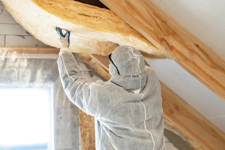 Back view of one foreman in overalls working with rockwool insulation material, fasten warmth layer on ceiling and wall, standing inside new house under construction