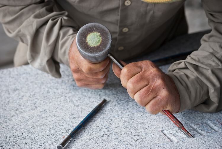 Stone mason doing some letters on a granite stone