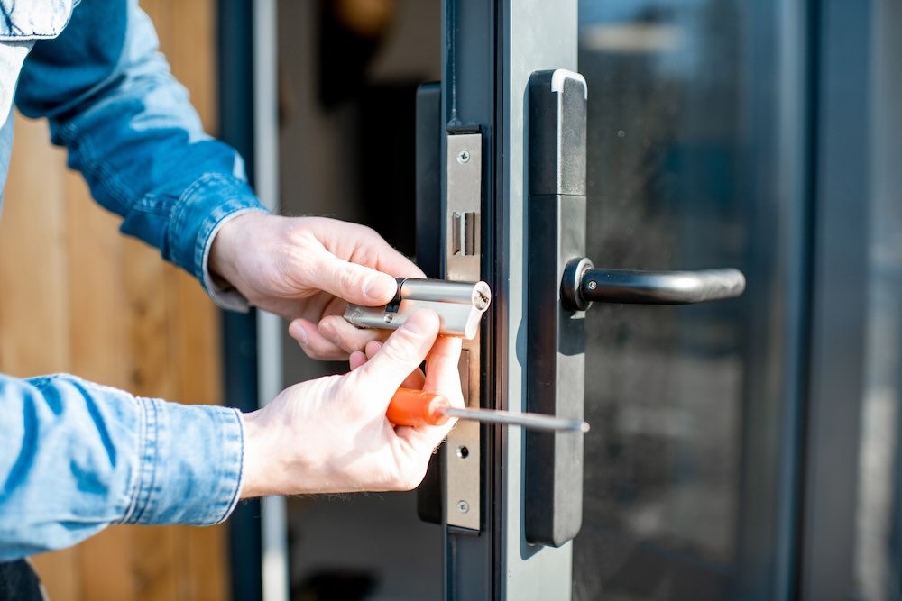 Insured locksmith changing core of a door lock of the entrance glass door, close-up view with no face