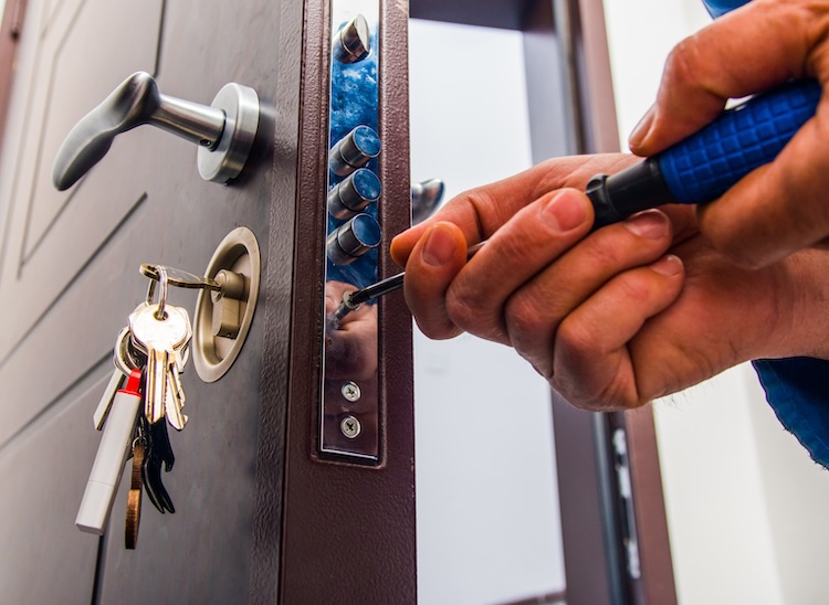 Locksmith with public liability is standing in the hallway and fixing the door lock with screwdriver