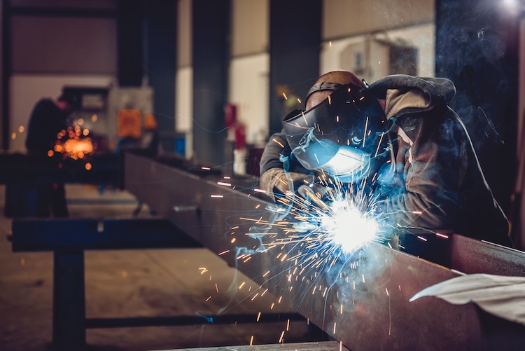 Industrial Welder With Torch and Protective Helmet in big hall welding metal profiles