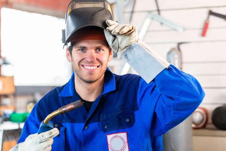 Insured welder with welding device in metal workshop looking into camera