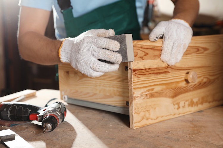 Professional cabinet maker polishing wooden drawer in workshop, closeup