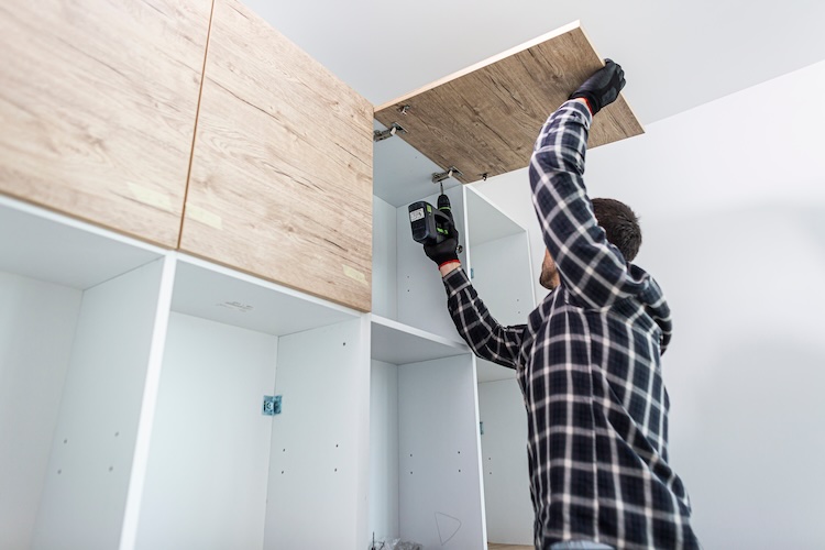 The cabinet maker sets and screws the mechanisms (joints) of the kitchen shelf door.